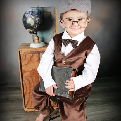 Young boy in vintage attire holding a book beside a globe